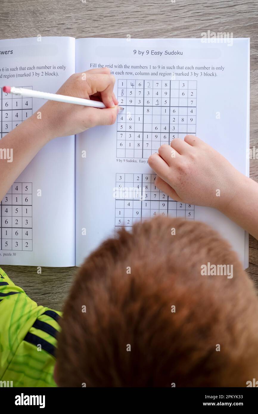 Un niño que completa un libro de ejercicios de Sudoku para jóvenes. La imagen muestra un rompecabezas Sudoku de 9 x 9 que es parcialmente completado por el joven Foto de stock