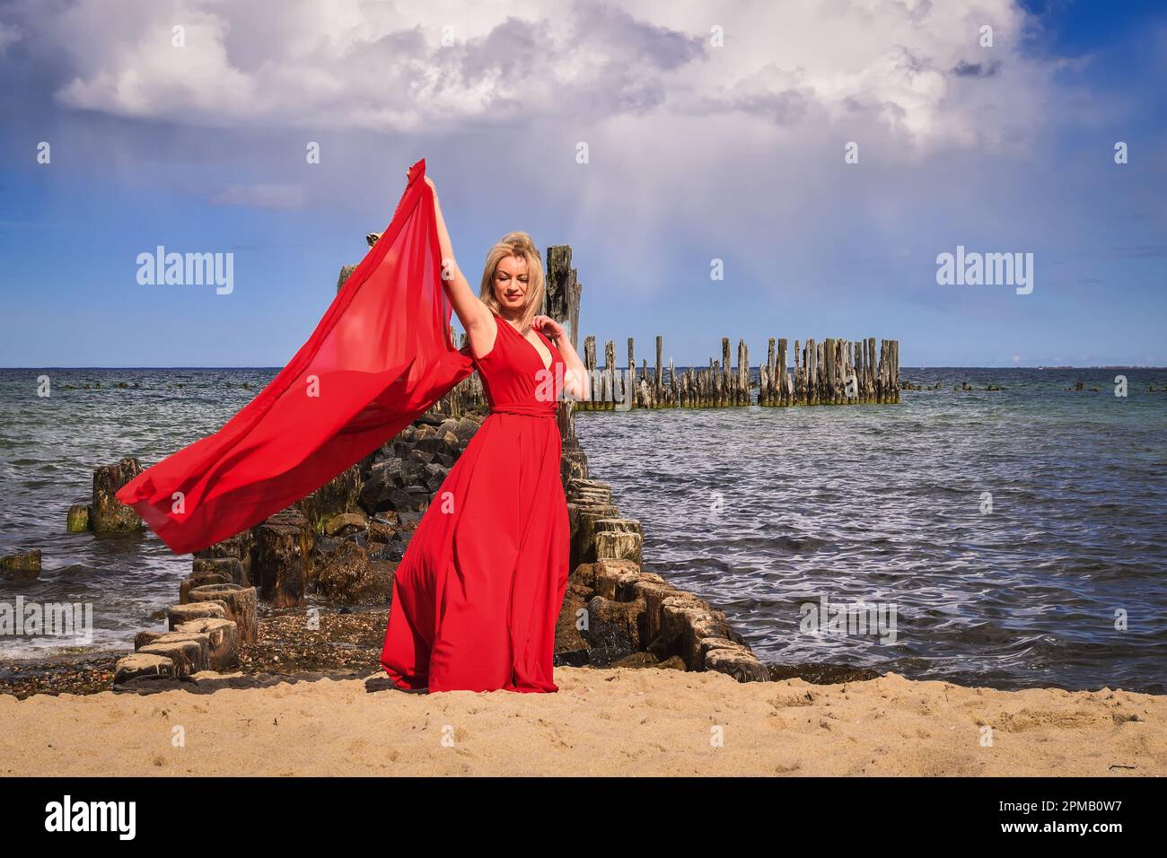 Interesante concepto de vacaciones con una mujer de pelo rubio en la playa.  Hermosa mujer en un vestido rojo en las orillas del mar Báltico en Gdynia,  Polonia Fotografía de stock -