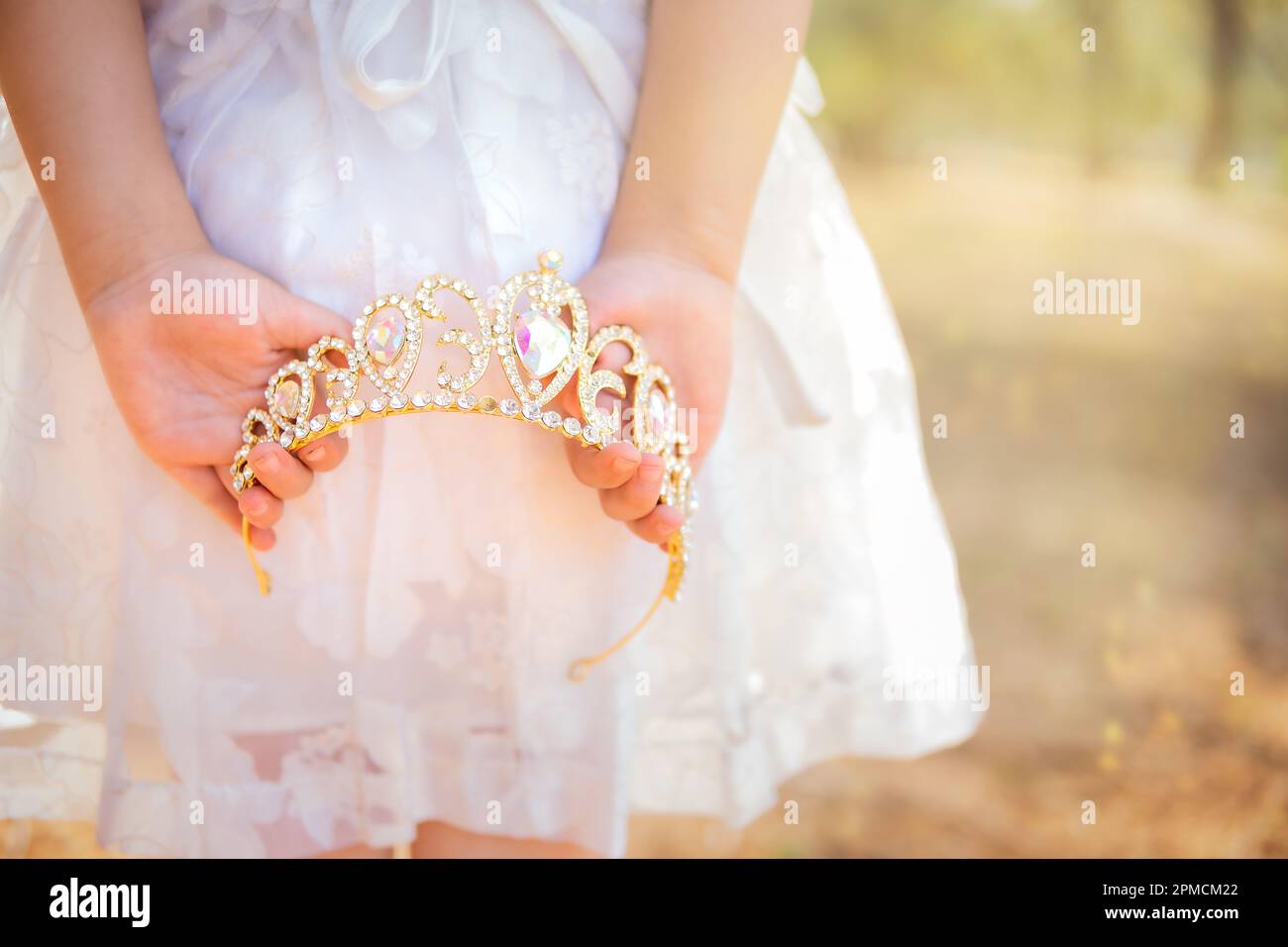 Niña en vestido blanco está en su espalda sosteniendo una corona de princesa, en un bosque de ensueño, espacio de copia, tema del día de los niños. Foto de stock