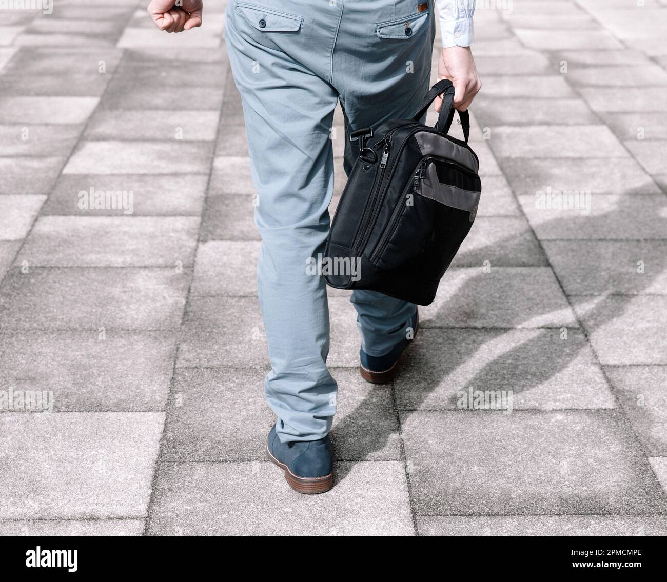 Hombre de negocios en un traje de color claro y maletín oscuro que va a trabajar, vista trasera Foto de stock