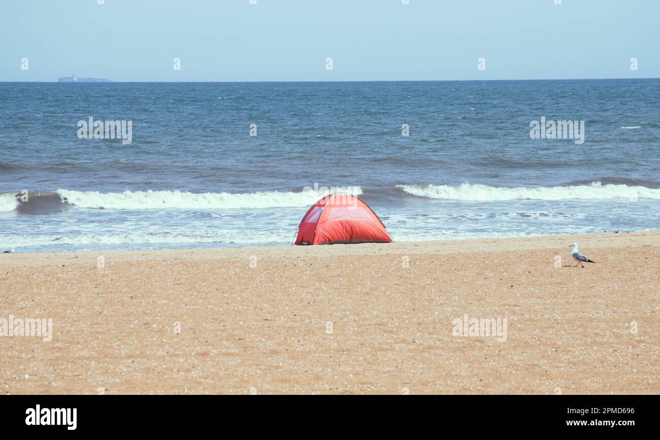 Una tienda de campaña naranja se estableció en la playa de arena, con olas rodando en el fondo de Virginia Beach, EE.UU.. Foto de stock