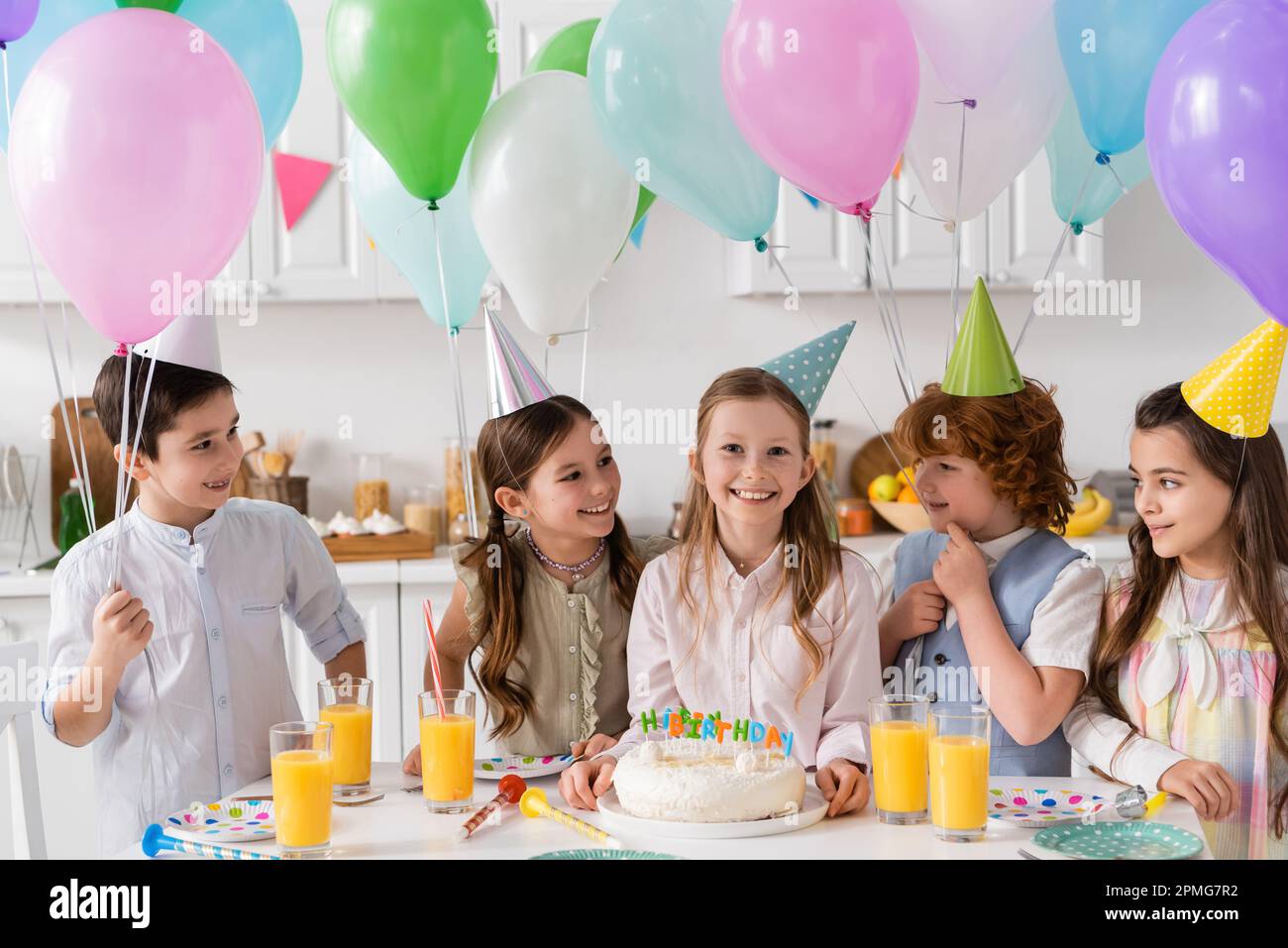 grupo de niños felices en gorras de fiesta que se divierten durante la celebración de cumpleaños junto a globos en casa, imagen de stock Foto de stock