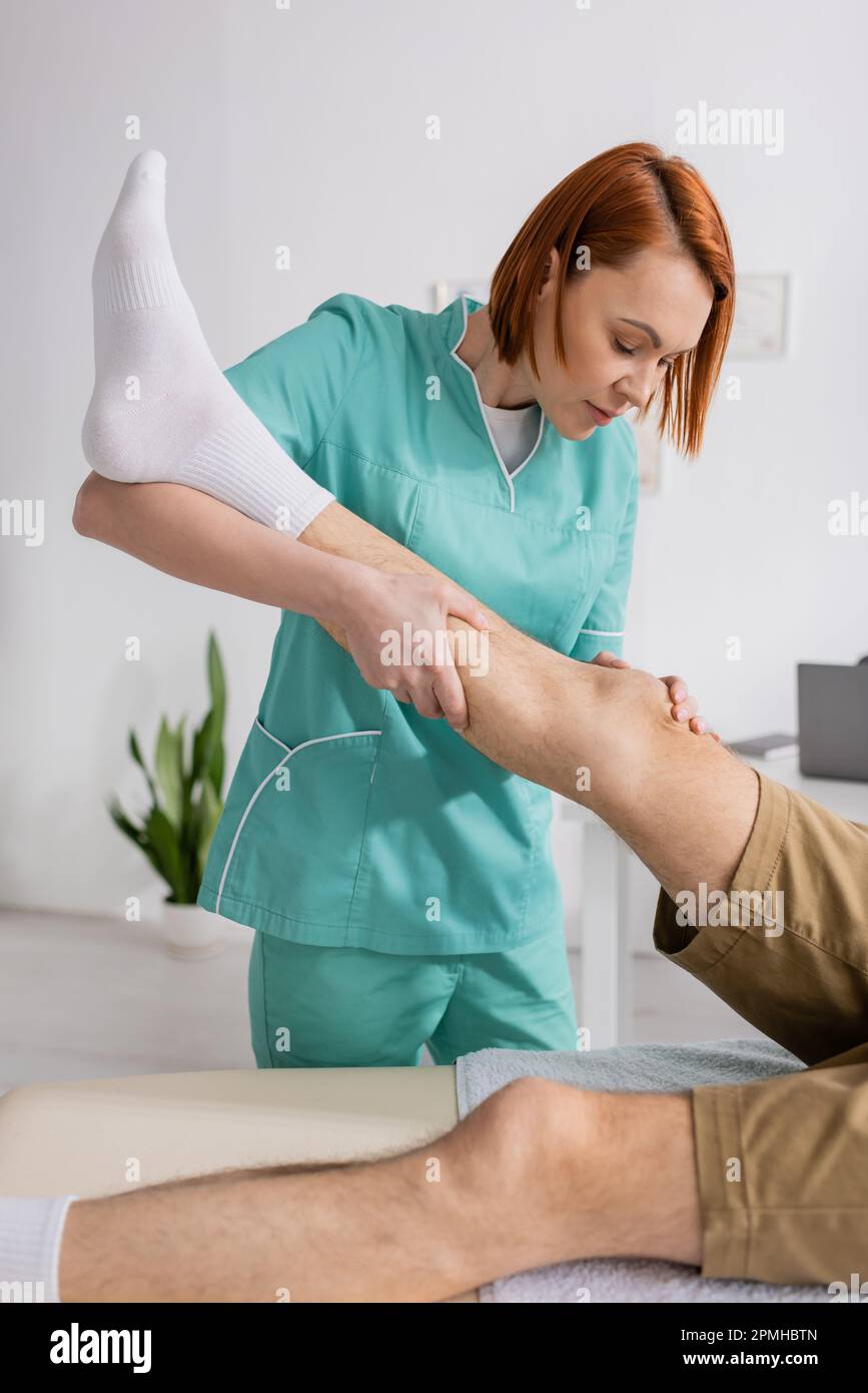 fisioterapeuta que estira la pierna del hombre herido durante la terapia de la rehabilitación en la sala de consulta, imagen de stock Foto de stock