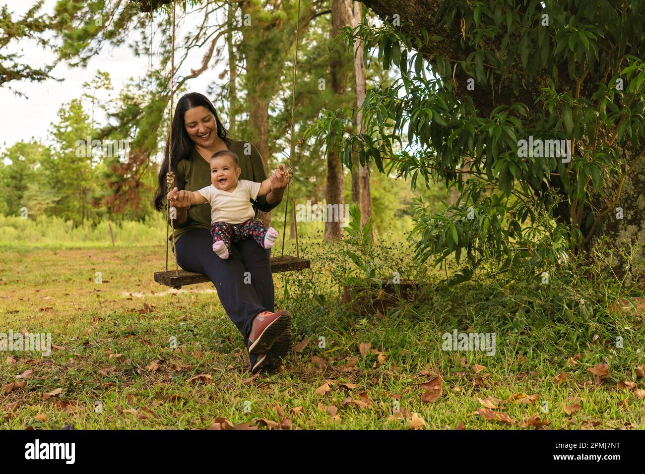 Feliz alegre linda niña sentada en un columpio con su madre jugando en el patio de recreo. Foto de stock