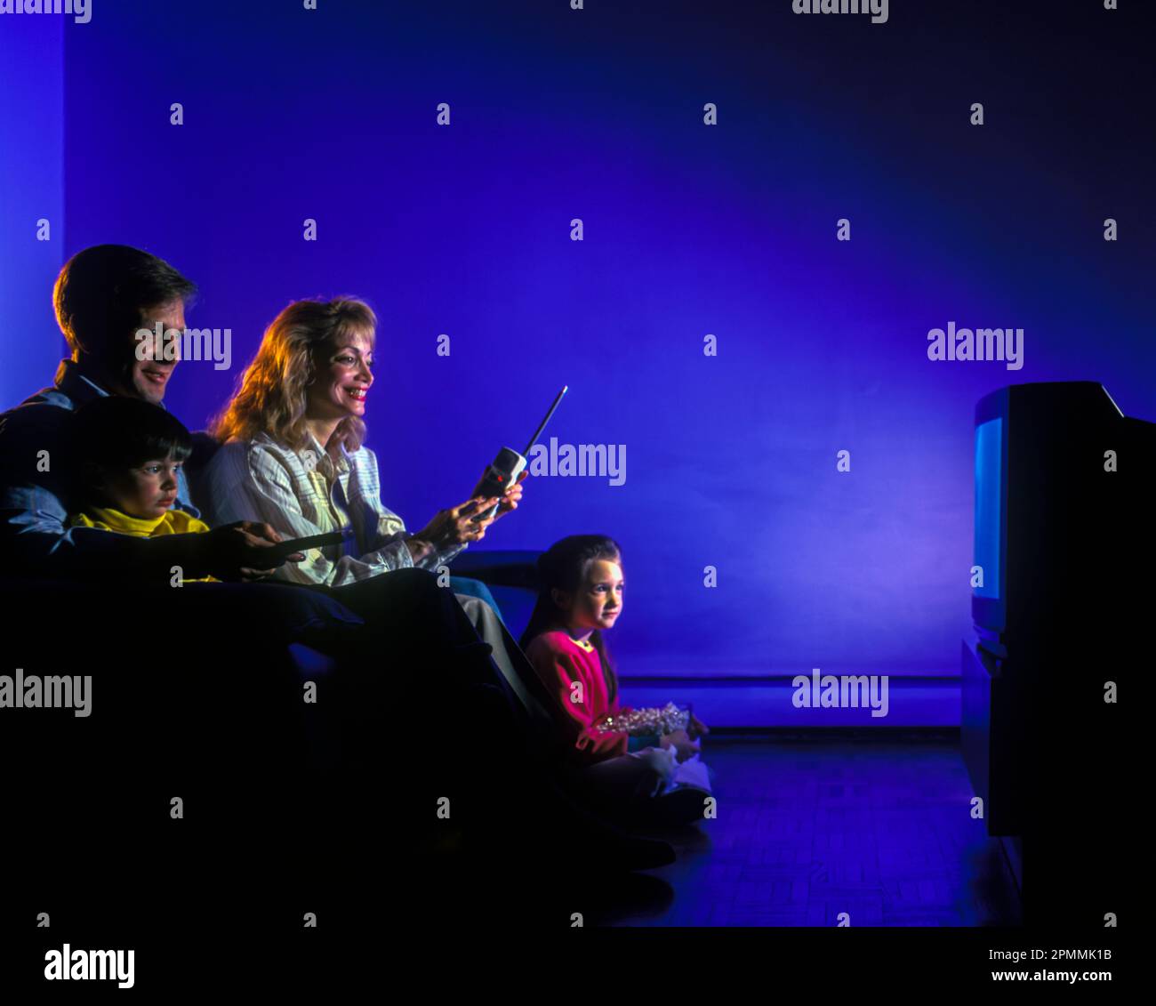 1994 FAMILIA HISTÓRICA SENTADA JUNTOS EN EL SOFÁ VIENDO LA TELEVISIÓN CRT ORDENANDO PAGO POR VISIÓN CON TELÉFONO Foto de stock