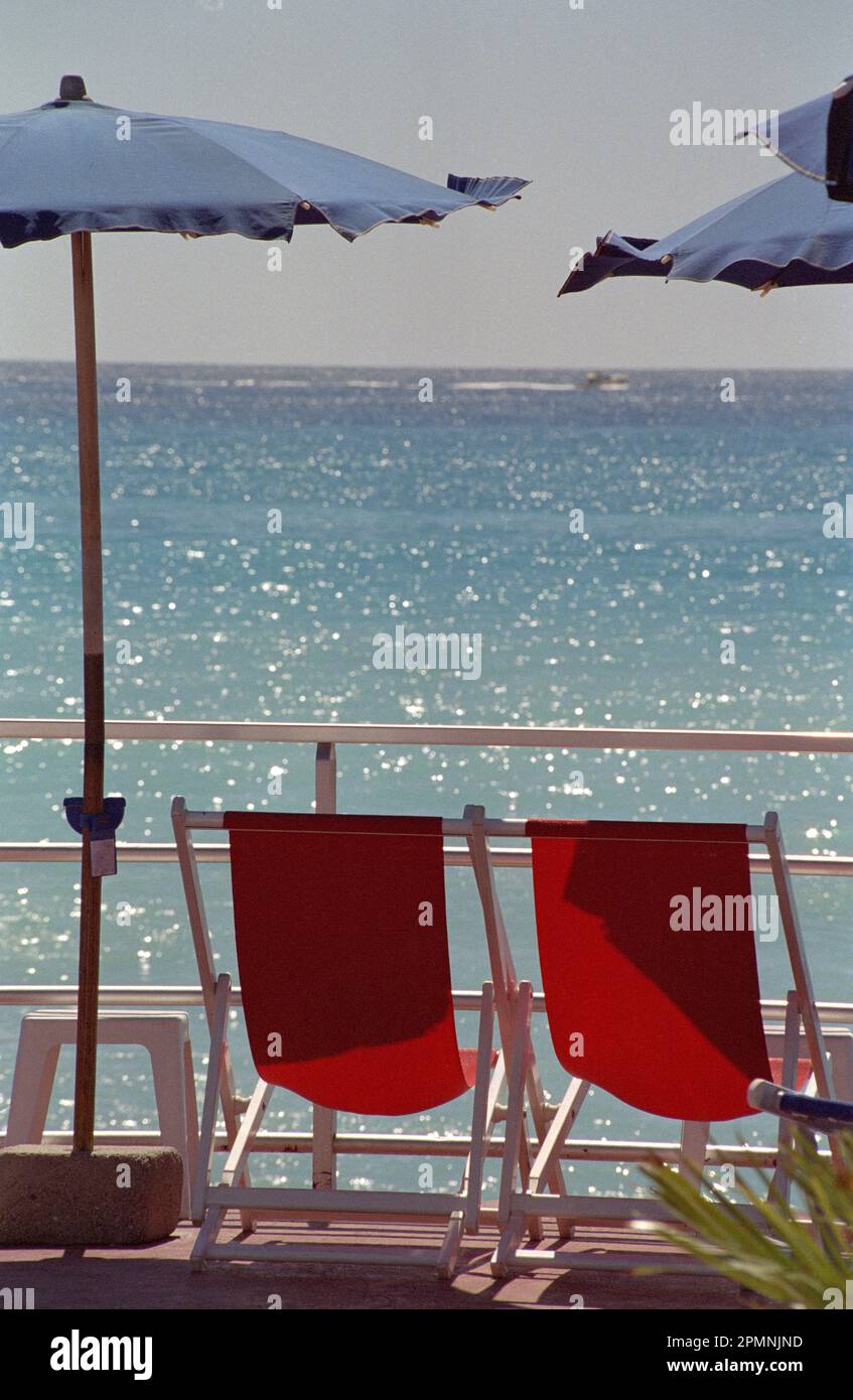 DOS SILLAS DE SOL ROJO Y SOMBRILLAS AZULES FRENTE AL MAR MEDITERRÁNEO BAJO  UN SOL BRILLANTE - PELÍCULA DE PLATA COLOR - ITALIA © FOTOGRAFÍA : FRÉDÉRIC  BEAUMONT Fotografía de stock - Alamy