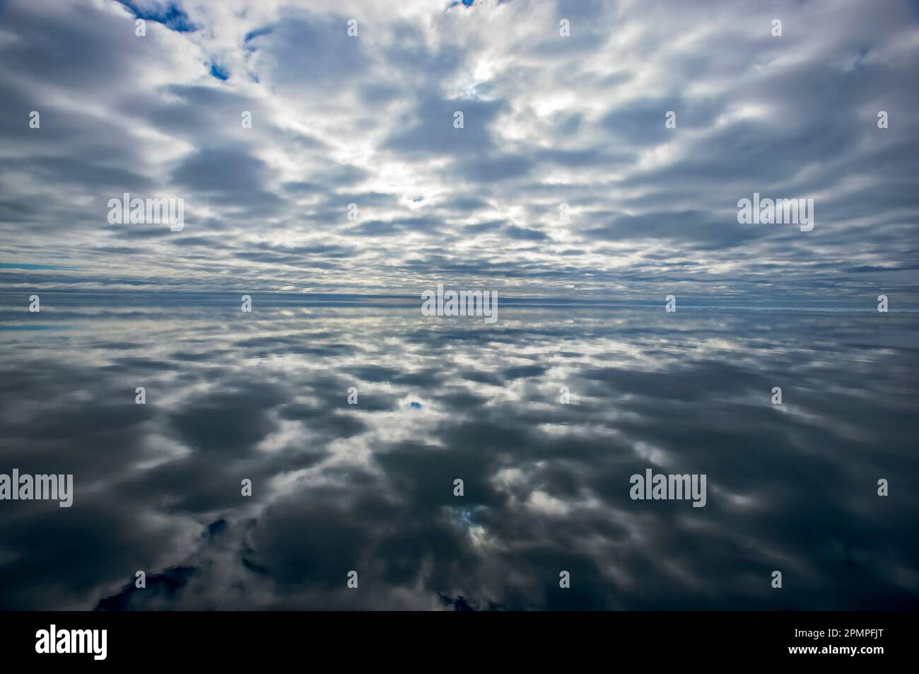 Imagen de espejo de un cielo nublado reflejado en la superficie del agua del océano; Archipiélago de Svalbard, Noruega Foto de stock