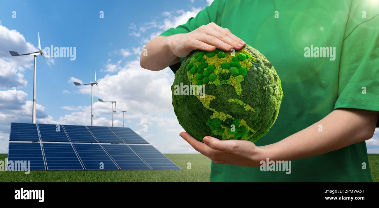 Mujer que sostiene un planeta verde Tierra sobre un fondo de turbinas de viento y paneles solares. Foto de stock