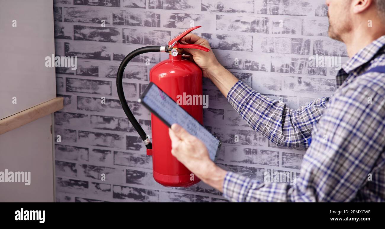 Trabajador que instala el extintor de incendios. Servicio de inspección. Comprobando etiqueta de seguridad Foto de stock