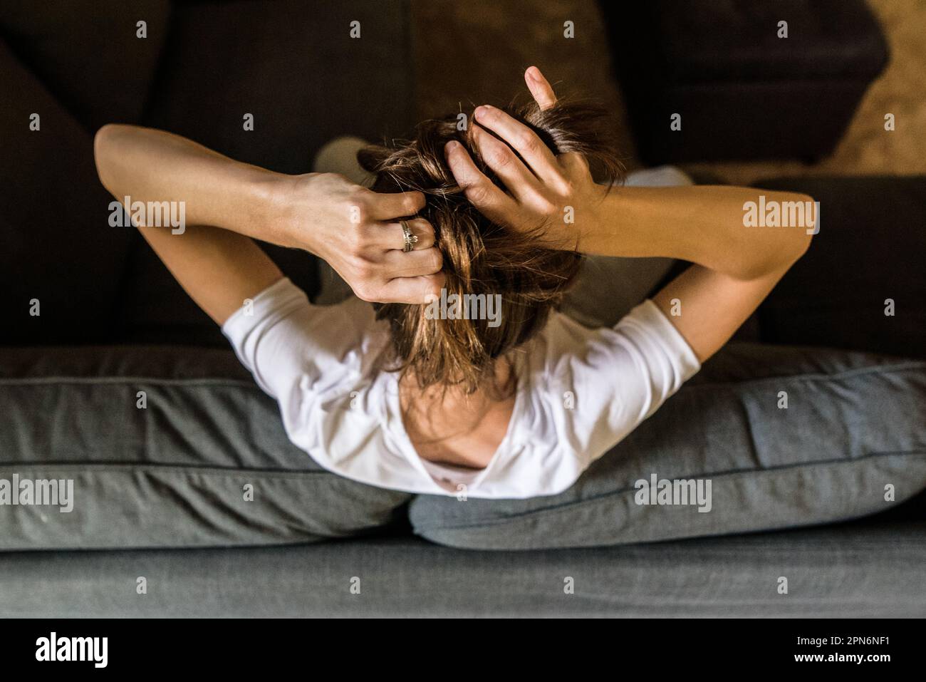 Mujer joven que se sienta en el sofá poniendo el pelo arriba desde arriba Foto de stock