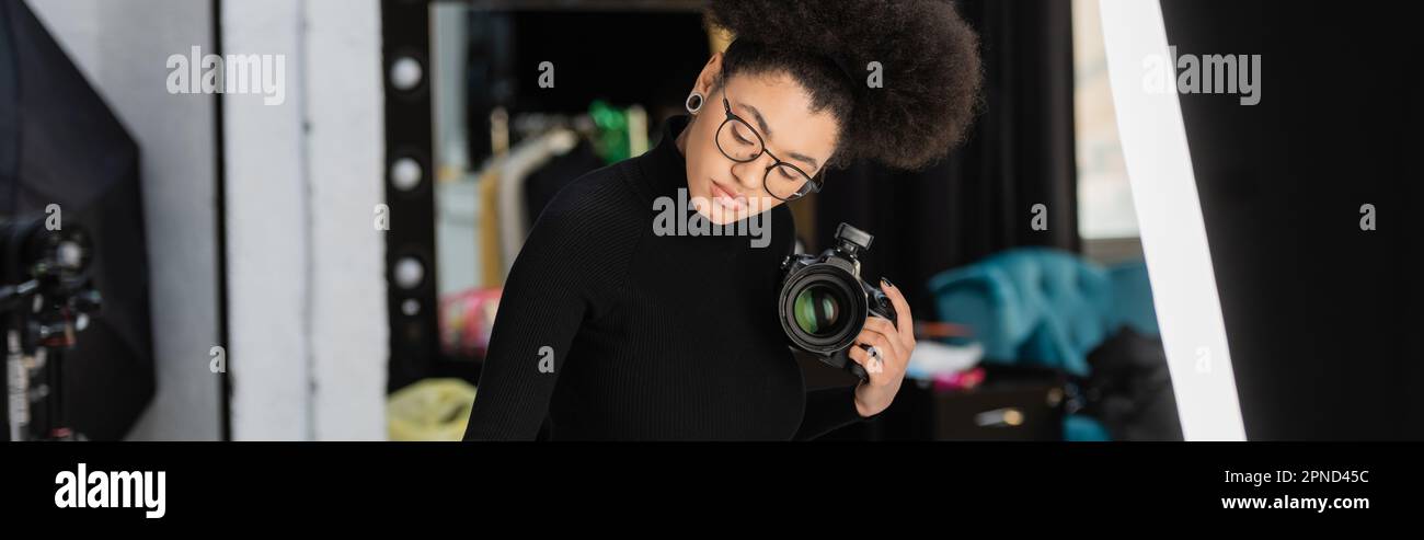 fotógrafo afroamericano en anteojos sosteniendo cámara digital profesional  en estudio fotográfico, banner, imagen de stock Fotografía de stock - Alamy