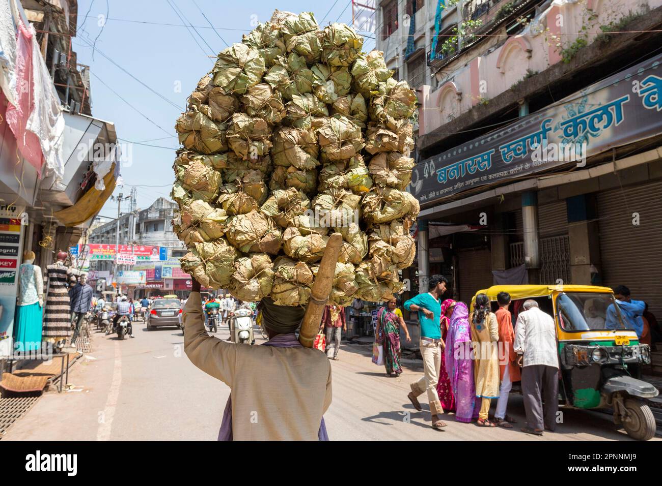 Un hombre lleva una carga pesada en su cabeza, transportando mercancías en la ciudad sagrada hindú, Varanasi, Uttar Pradesh, India Foto de stock