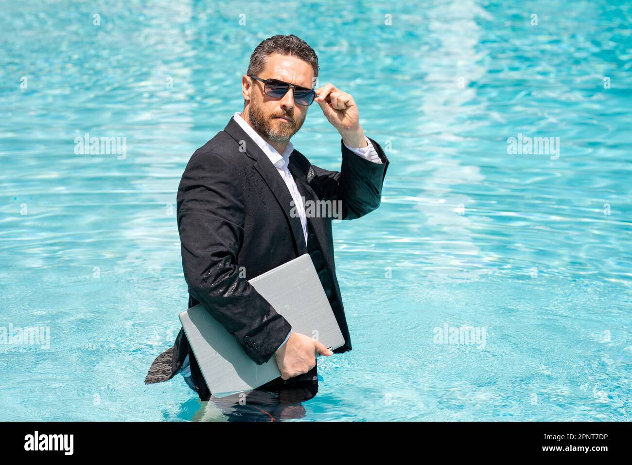 Joven hombre de negocios con gafas de sol trabaja en una computadora  portátil sentada en una mesa cerca de la piscina trabajo remoto freelancer
