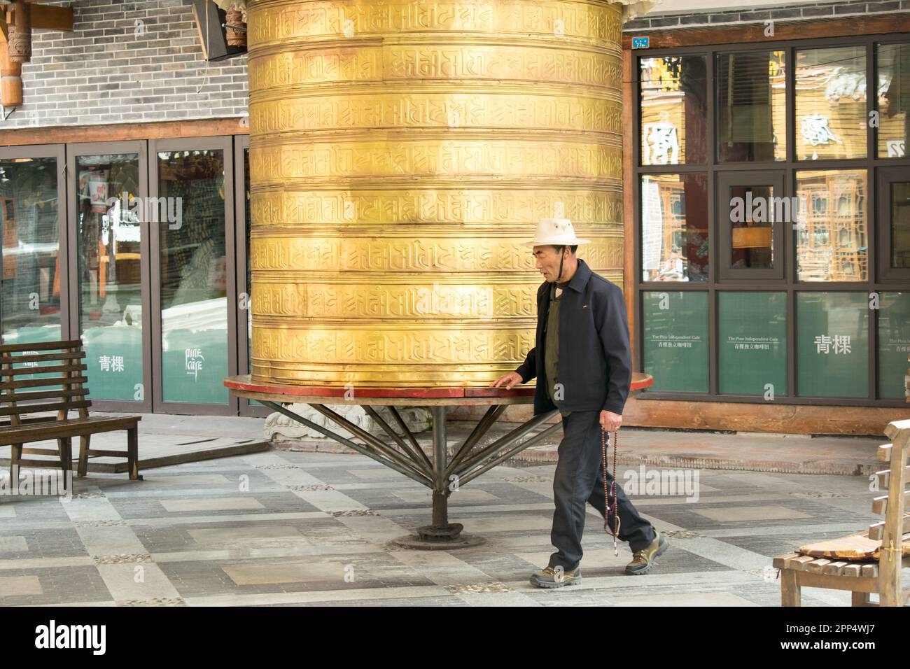 Un anciano tibetano hace girar una rueda de oración tibetana de tamaño humano - Kanding, China. Foto de stock