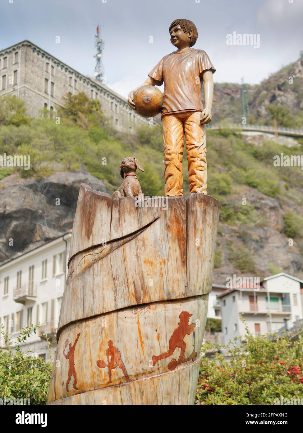 Estatua de madera de un niño con una pelota y un perro en un parque en la ciudad de Pont-Saint-Martin, Valle de Aosta, NW Italia Foto de stock