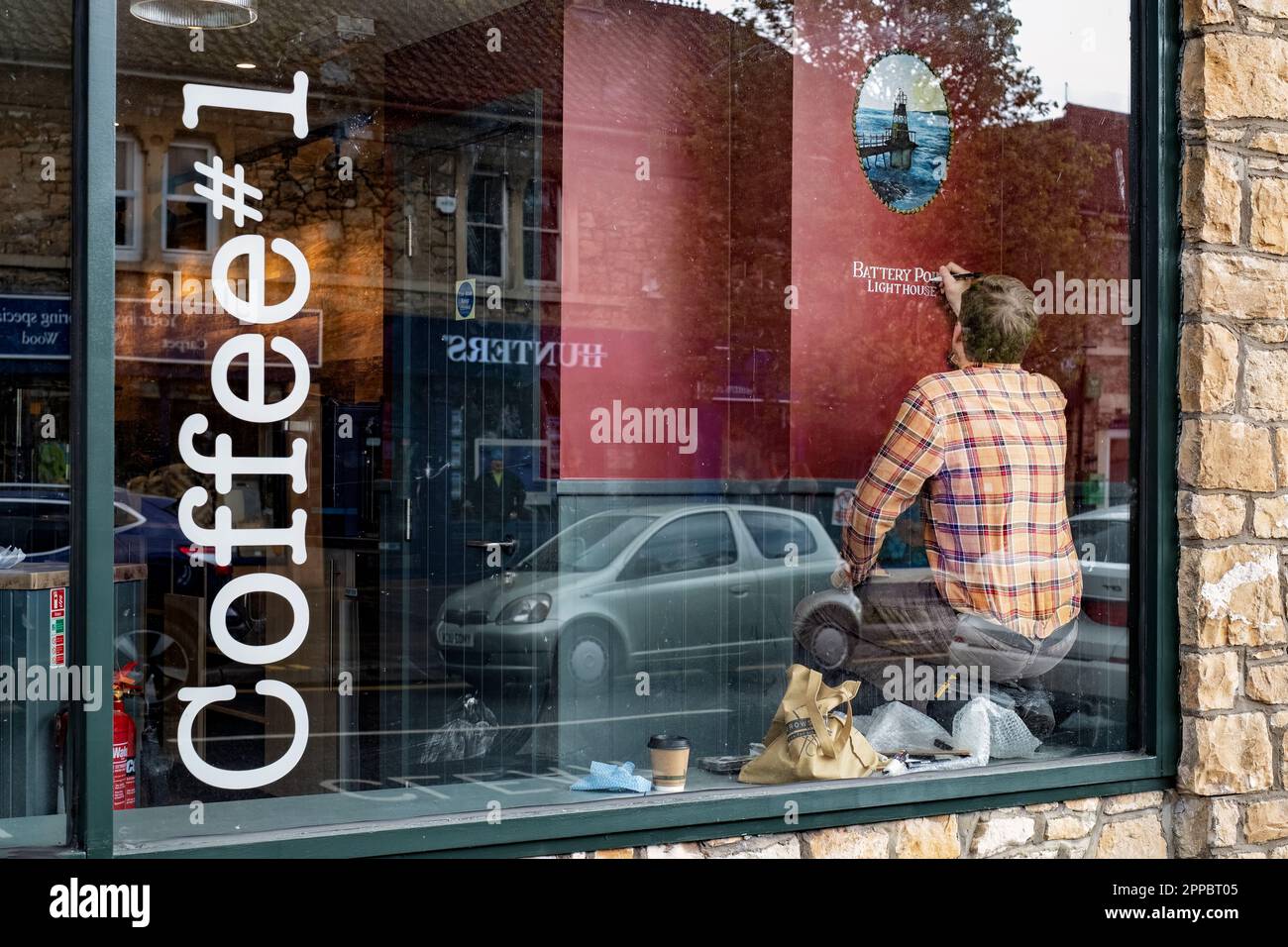 Un artista y escritor de letreros agrega algunos enlaces locales a un nuevo café no 1 que se instala en la tienda antes de la apertura. Coffee#1 es una cadena de café del reino unido Foto de stock