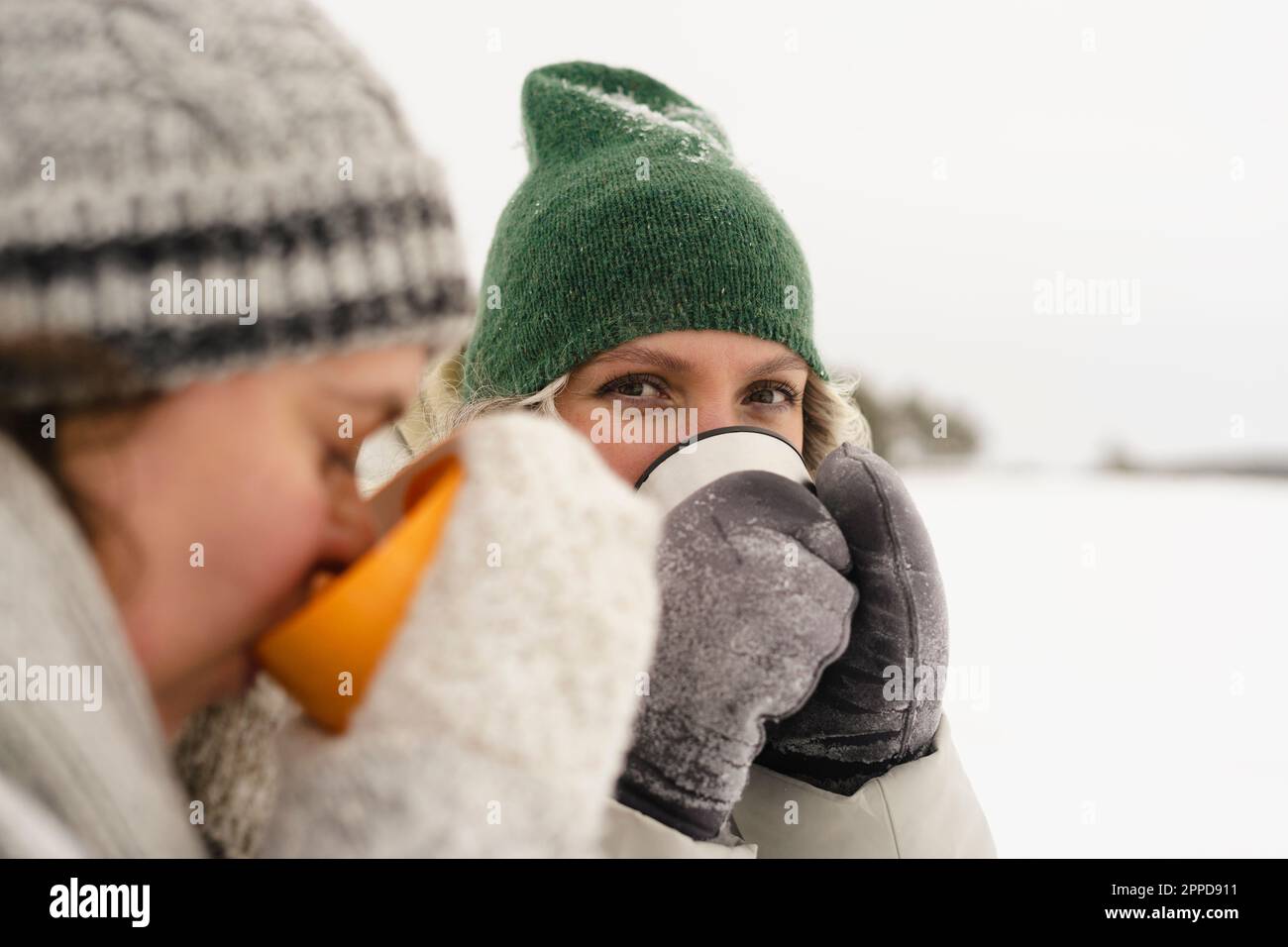 Mujer con gorro de lana de punto blanco disfrutando de un hermoso día de  nieve mientras bebe té caliente. nieve que cae