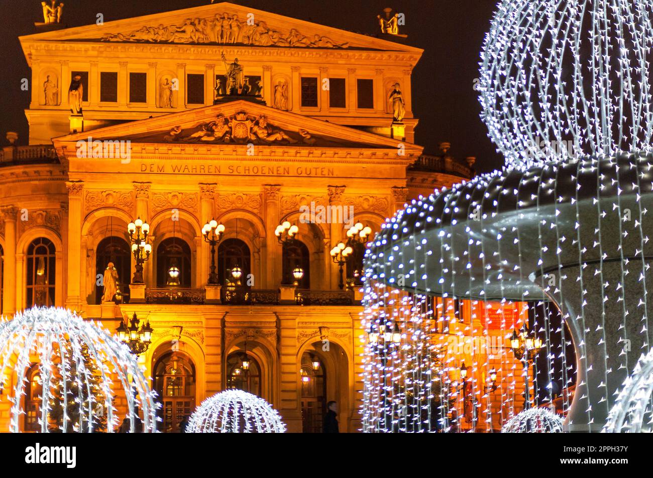 El punto de referencia 'Alte Oper' en Fráncfort del Meno con iluminación nocturna y el 'Lucaebrunen' con iluminación navideña festiva fotografiado desde un lugar público Foto de stock