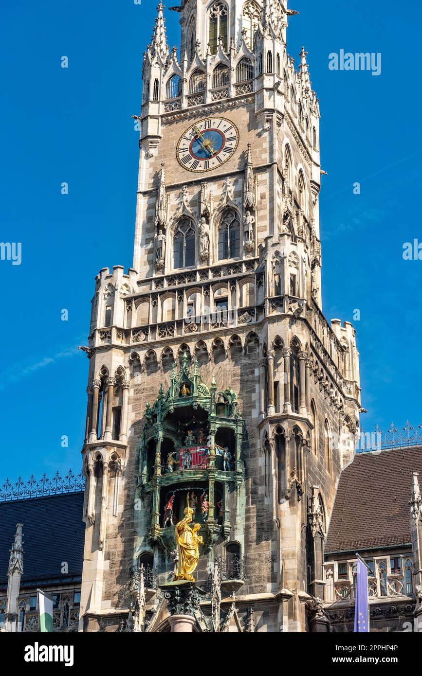 La fachada de estilo neogótico del nuevo ayuntamiento con la torre del ayuntamiento en el casco antiguo de Munich en la vista inferior vista desde Marienplatz en el hermoso clima de verano y el cielo azul con las dos torres de la Frauenkirche en el fondo Foto de stock