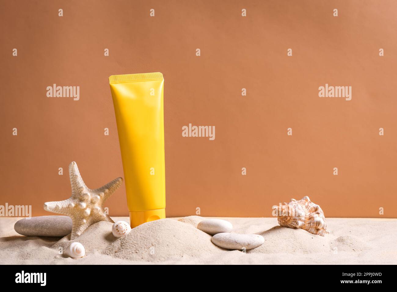 Bloqueador solar en tubo cosmético naranja en arena de playa y fondo beige, vista lateral, espacio de copia. Vacaciones de verano y concepto de cuidado de la piel con estrellas de mar y se Foto de stock