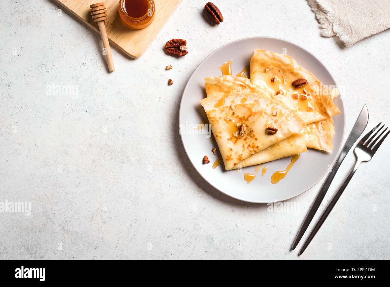 Crepes Suzette con miel y nueces de pacana sobre fondo blanco. Deliciosos crepes caseros para el desayuno. Foto de stock