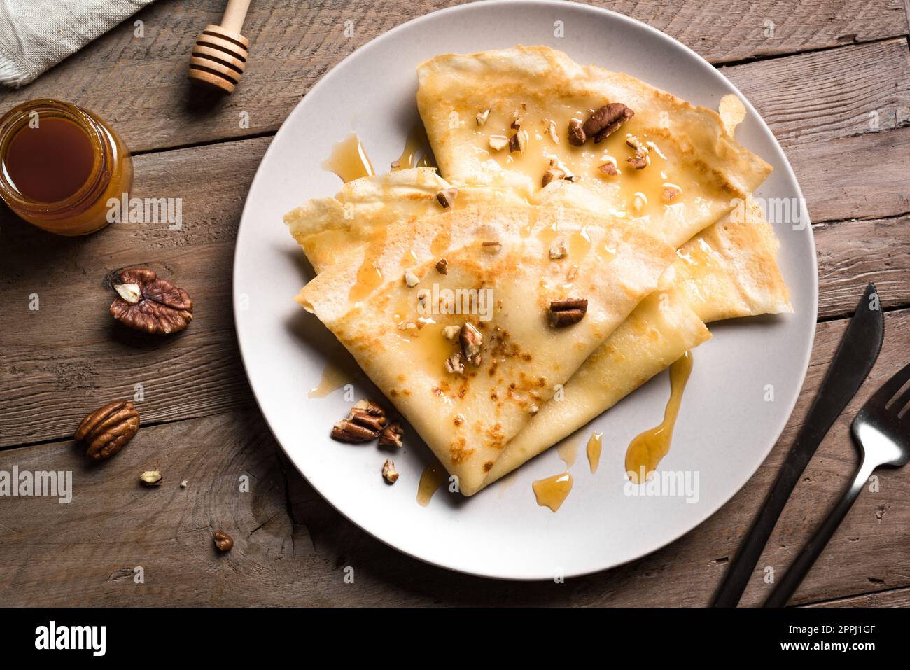 Crepes Suzette con miel y nueces de pacana sobre fondo de madera cerca. Crepes caseros para el desayuno o el postre. Foto de stock