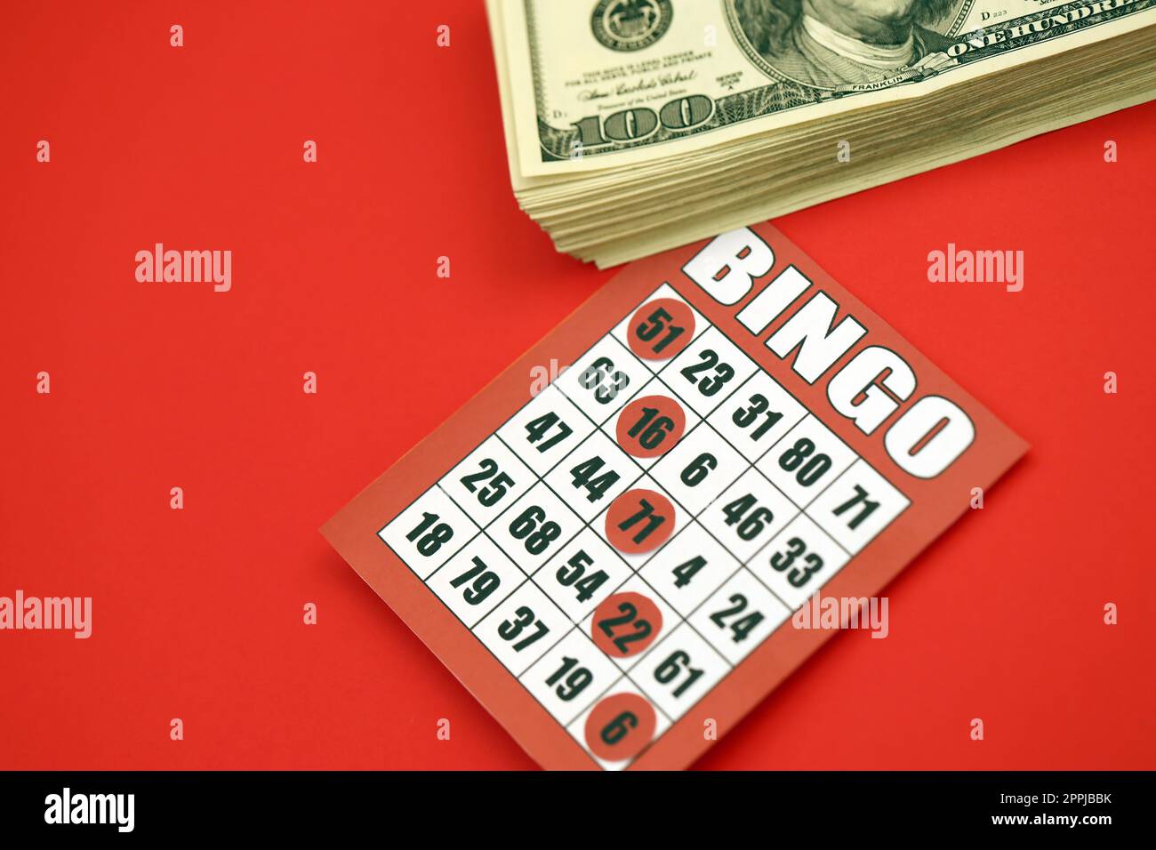 Tablero de bingo rojo o tarjeta de juego para ganar fichas y pila de billetes de dólar. Clásico americano o canadiense cinco a cinco tarjeta de bingo sobre fondo rojo Foto de stock