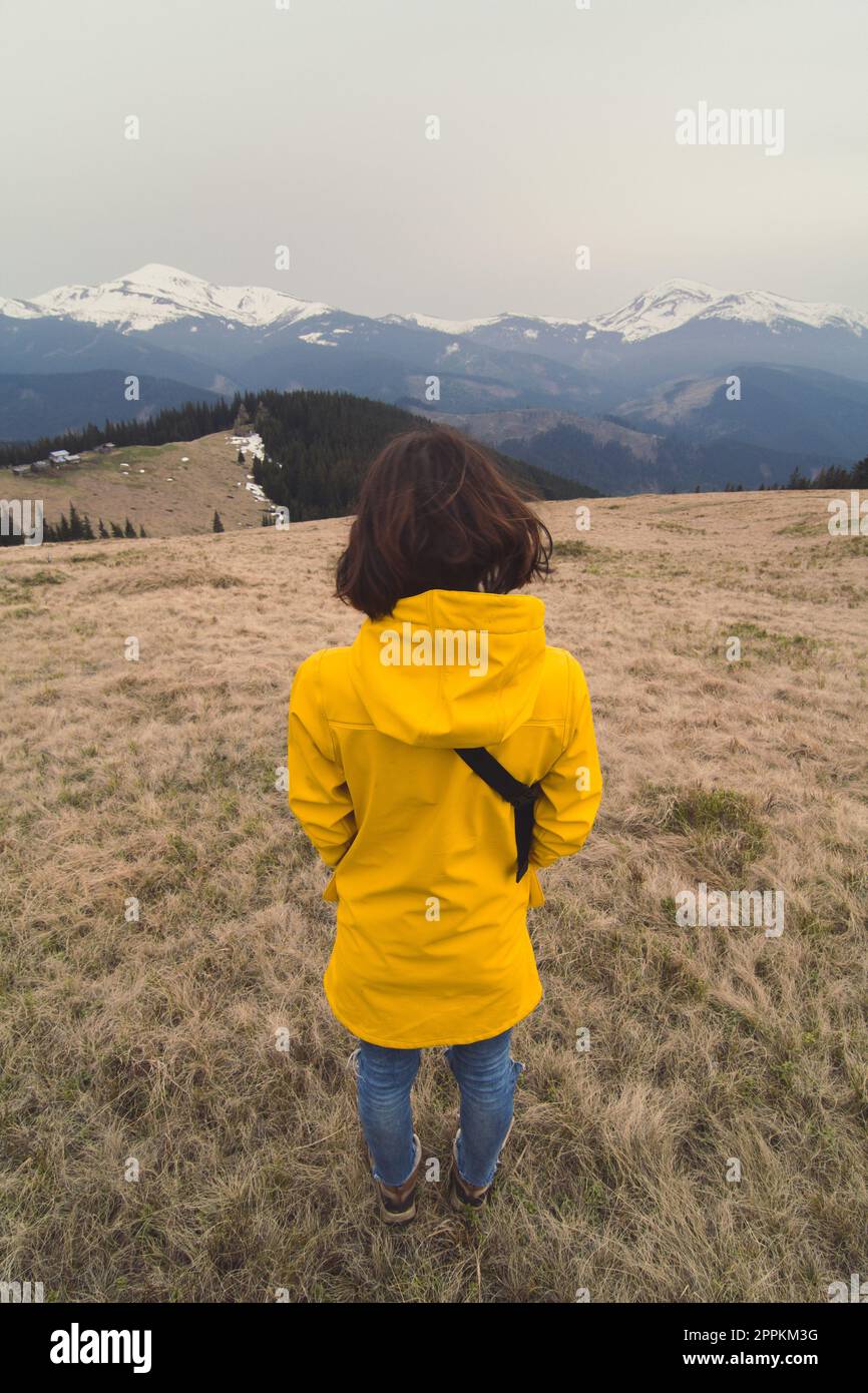 Close up mujer en abrigo amarillo mirando la foto de concepto de picos montaña nevados. Fotografía de vista posterior con paisaje fondo. Imagen de alta calidad Fotografía de stock -