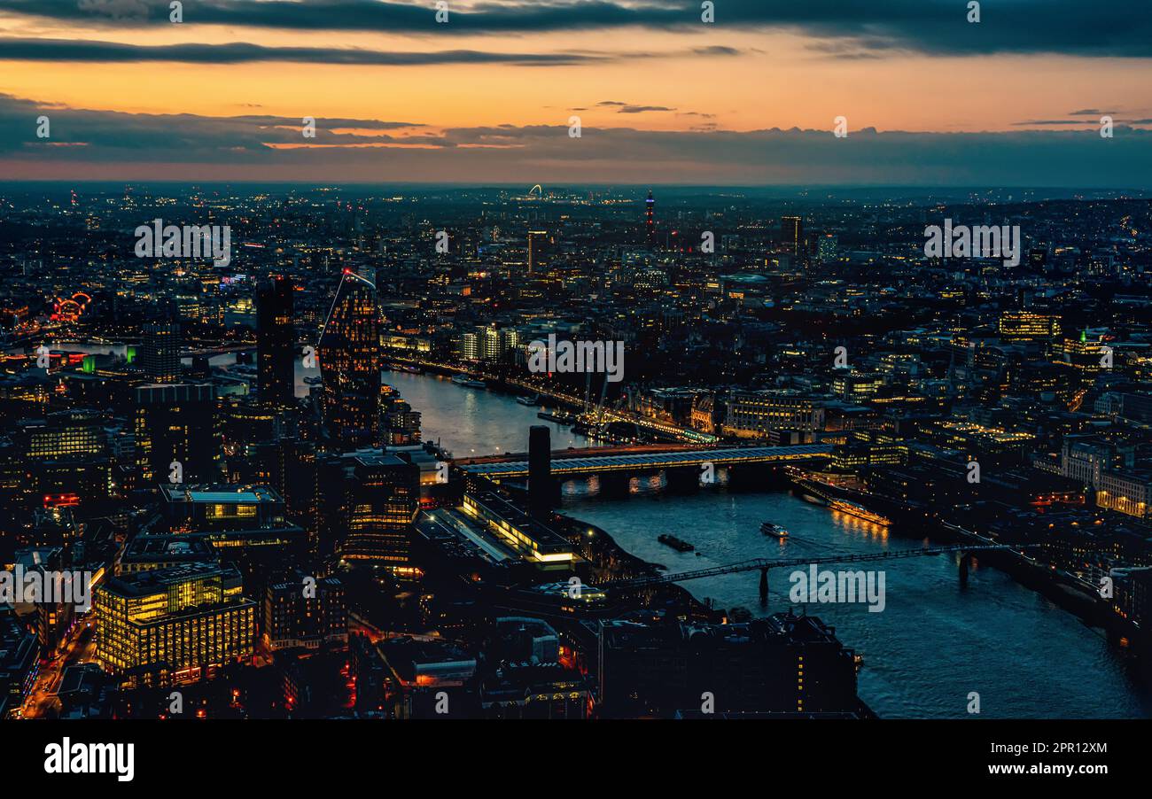 Vista aérea del oeste de Londres, hora azul justo después de la puesta del sol, luces de calle amarillas anaranjadas que comienzan a brillar, río Támesis que separa dos orillas Foto de stock