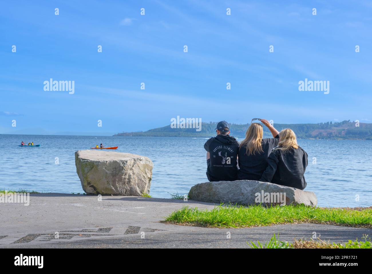 Taupo Nueva Zelanda - 16 2023 de abril; tres adultos jóvenes sentados junto al lago mirando a la vista. Foto de stock