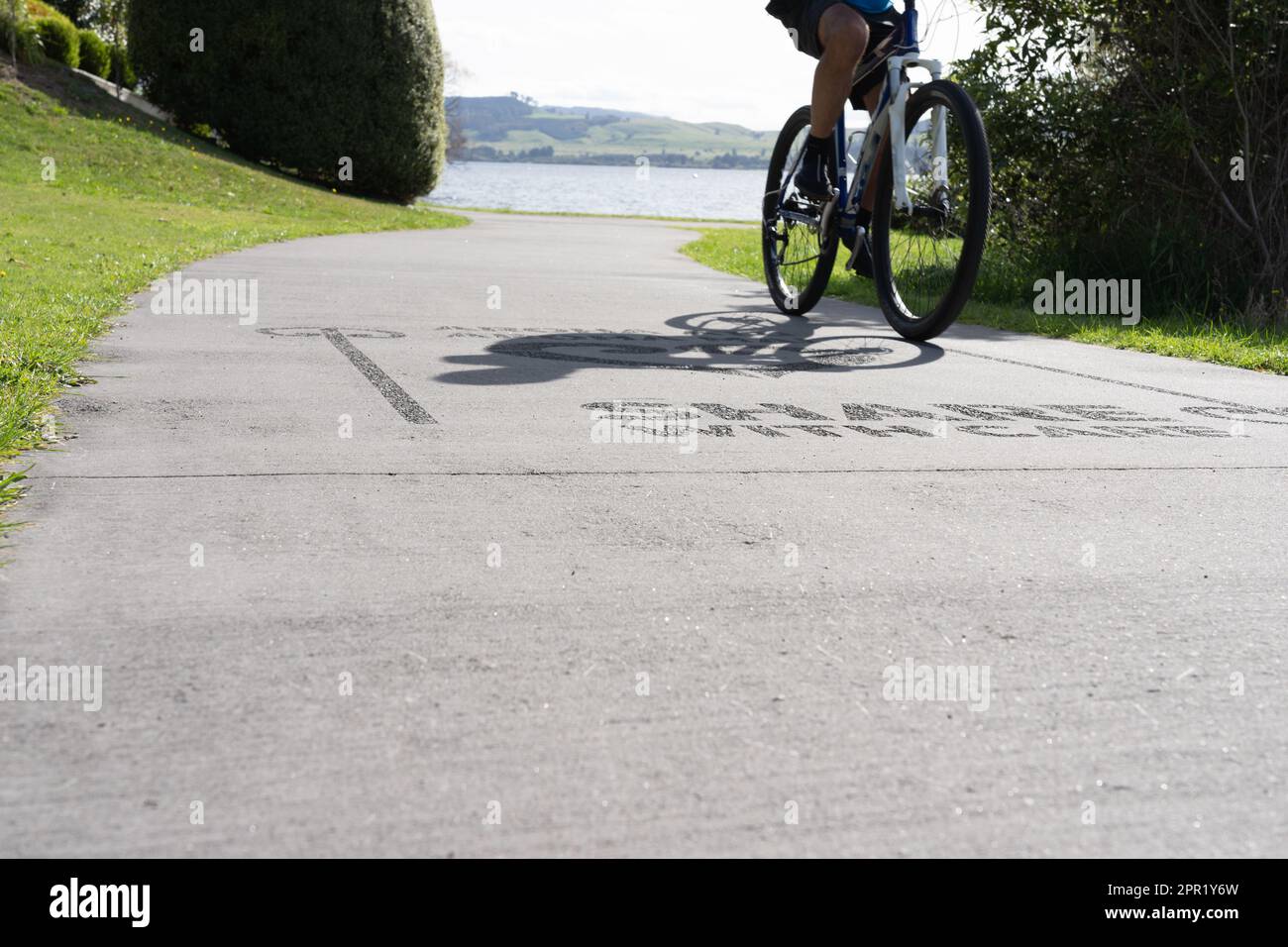 Silueta de borrosa en movimiento ciclistas en camino compartido con signo en la superficie 'Compartir con cuidado' alrededor de la orilla del lago Taupo. Foto de stock