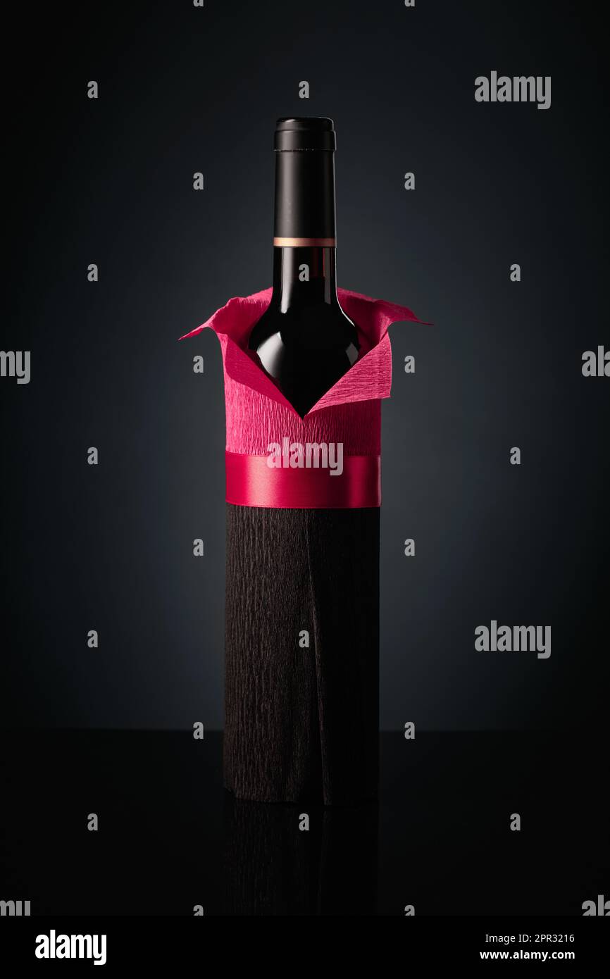 Botella de vino tinto envuelto en papel crepé sobre un fondo negro. La  botella parece un hombre con una camisa roja Fotografía de stock - Alamy