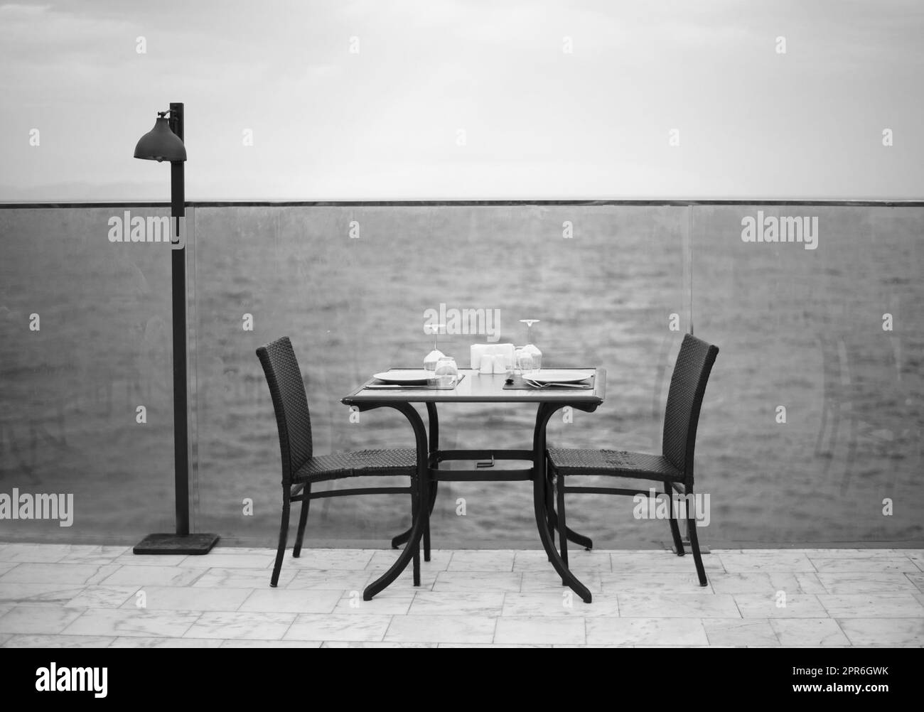 Increíble cena romántica en la playa. Romance y amor, mesa de comedor con vista al mar en el día nublado. Foto blanco negro Foto de stock