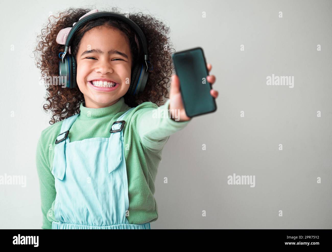 En cada gesto, dignidad y amor. Fotografía de una niña de pie sola y escuchando música a través de los auriculares sobre un fondo gris. Foto de stock
