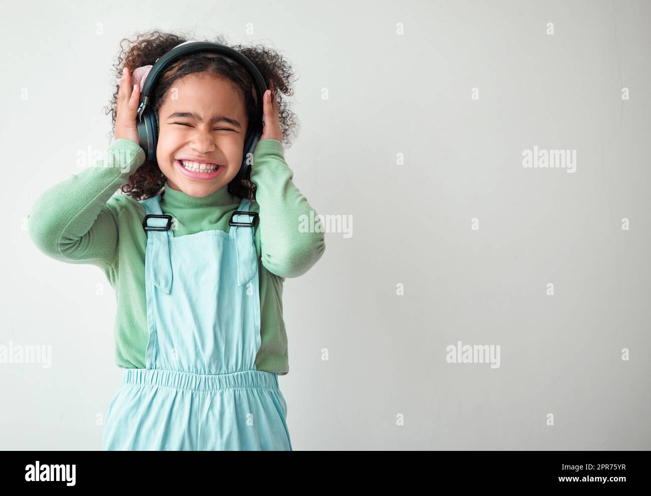 La gracia estaba en todos sus pasos. Fotografía de una niña de pie sola y escuchando música a través de los auriculares sobre un fondo gris. Foto de stock