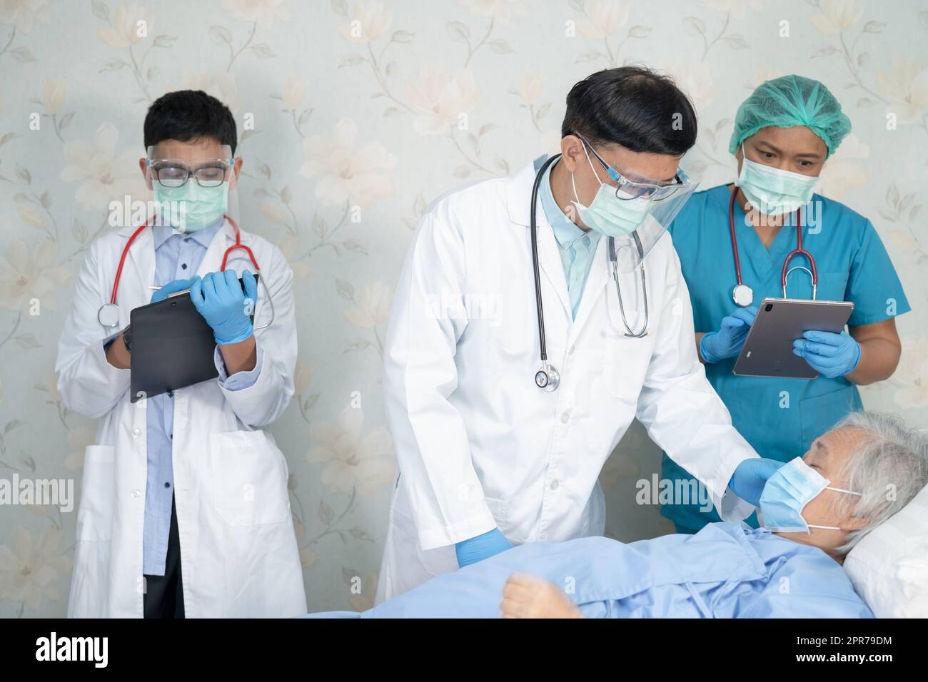 El equipo médico asiático comprueba la vieja paciente de la señora mayor para la enfermedad a la motivación normal nueva para tratar la infección Covid19 Coronavirus en la sala del hospital. Foto de stock