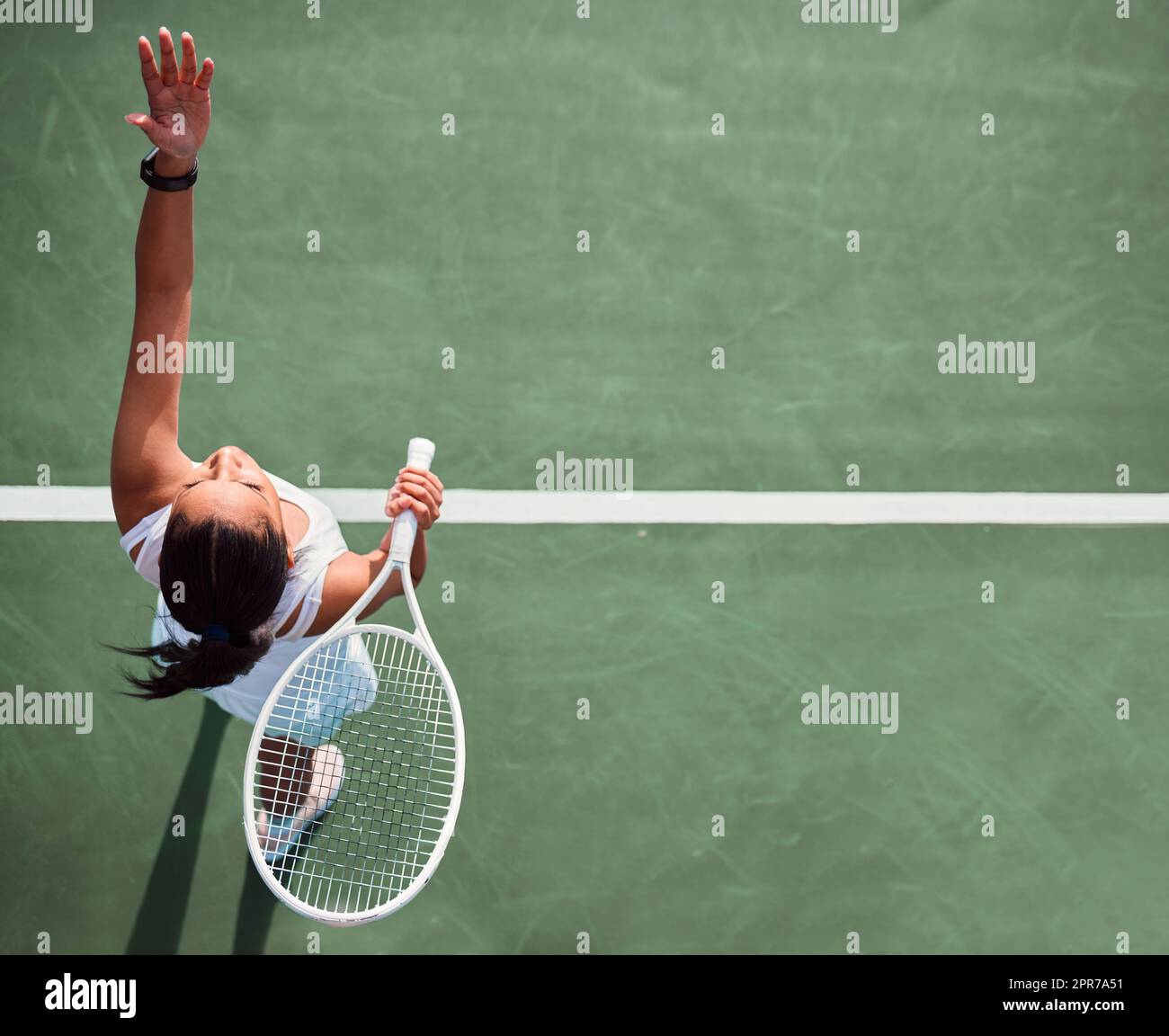 ¡A jugar! Disparo de ángulo alto de una mujer joven sirviendo una pelota mientras juega al tenis en una cancha. Foto de stock