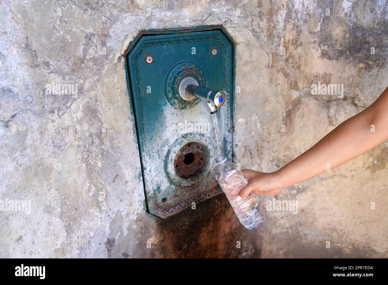 La mano de una mujer llena una botella de plástico de agua de una fuente en la pared. Sediento y crisis del agua. Foto de stock