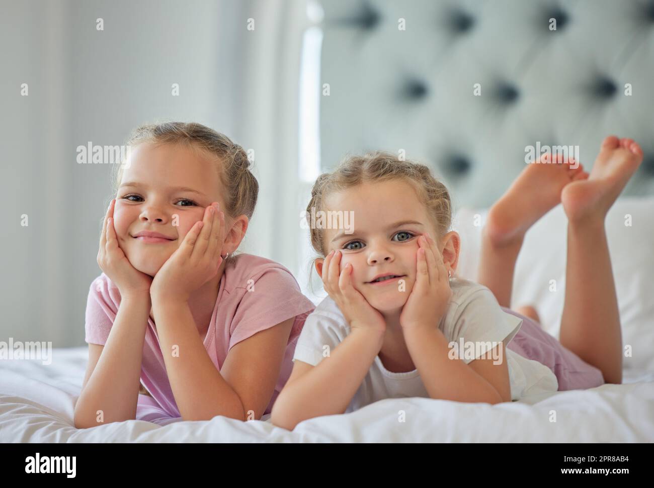 Retrato de dos niñas mintiendo en una cama en casa. Chicas sonrientes que solo se relajan y se ven cómodas, dos hermanas caucásicas rubias disfrutan del tiempo en la cama juntas en un dormitorio luminoso en casa Foto de stock