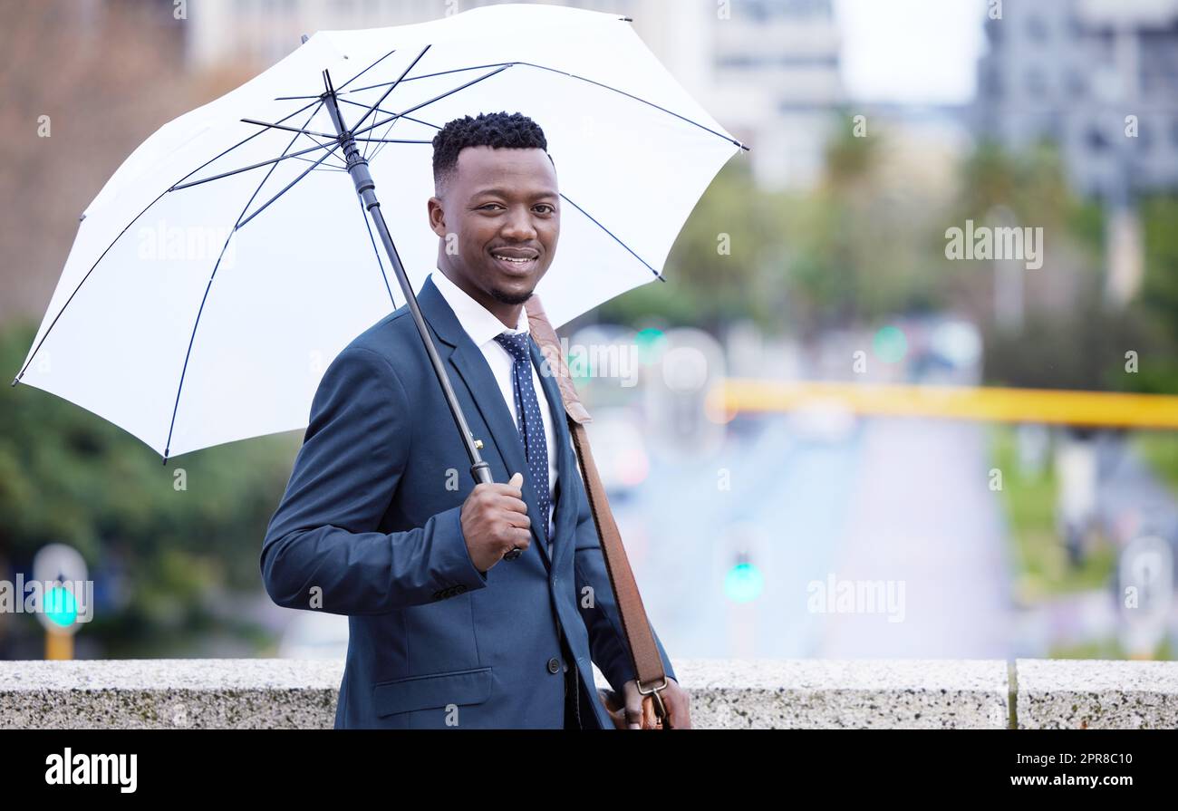 Tengo que mantenerme cubierto de la lluvia. Un joven hombre de negocios sosteniendo un paraguas bajo la lluvia contra el fondo de la ciudad. Foto de stock