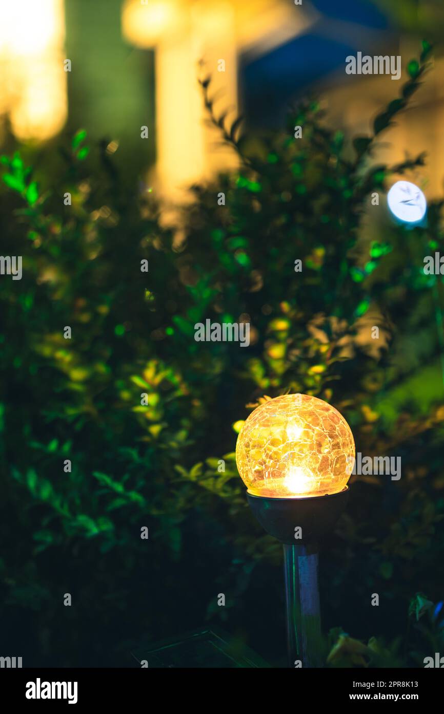 Vista nocturna del macizo de flores iluminado por linterna multicolor de energía solar de ahorro de energía en el patio. Hermoso pequeño jardín con luz amarilla, lámpara en cama de flores. Diseño de jardín Foto de stock