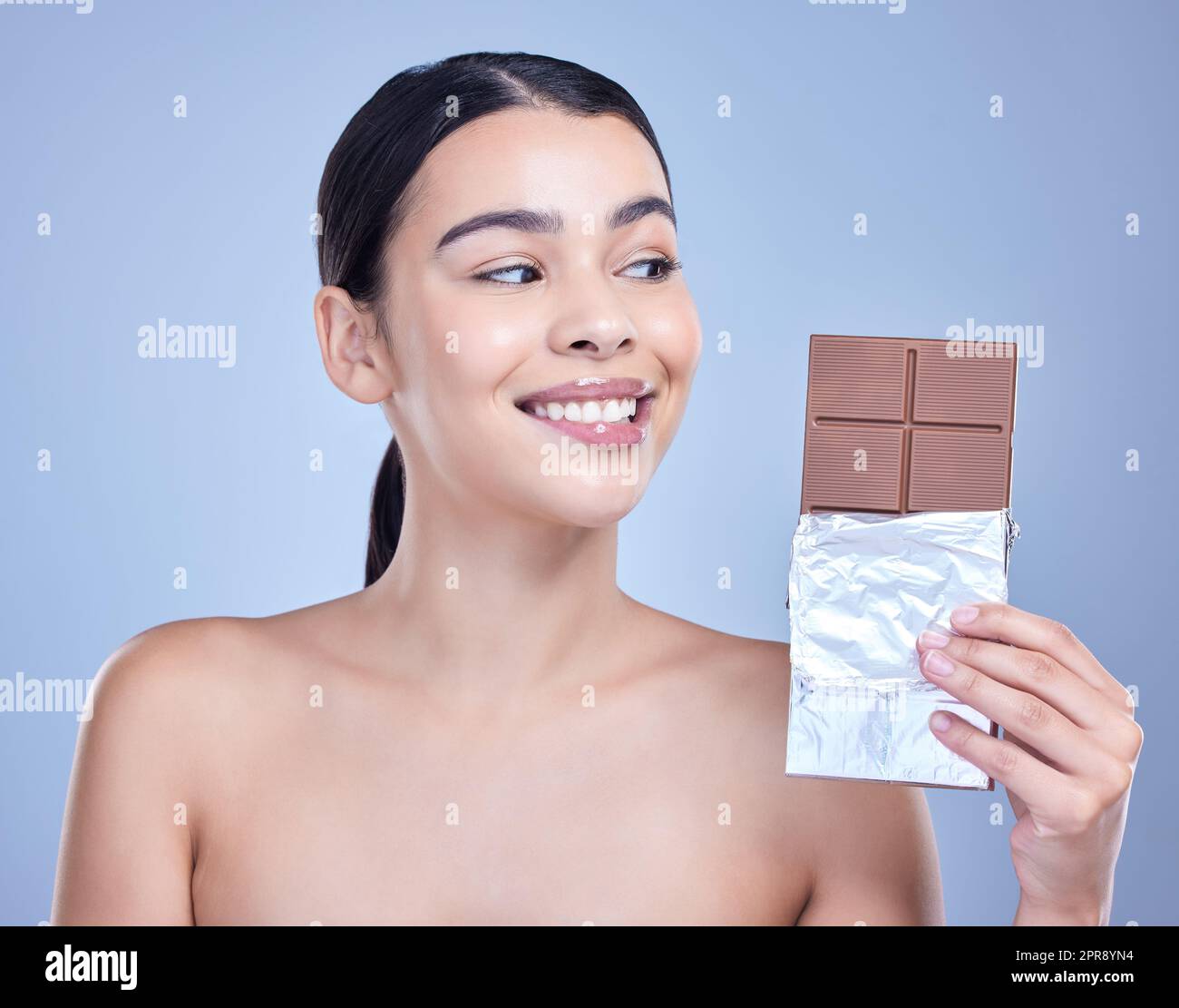 Una hermosa mujer de raza mixta sosteniendo una losa de chocolate. Bocado modelo hispano en el postre sobre un fondo azul de copyspace Foto de stock