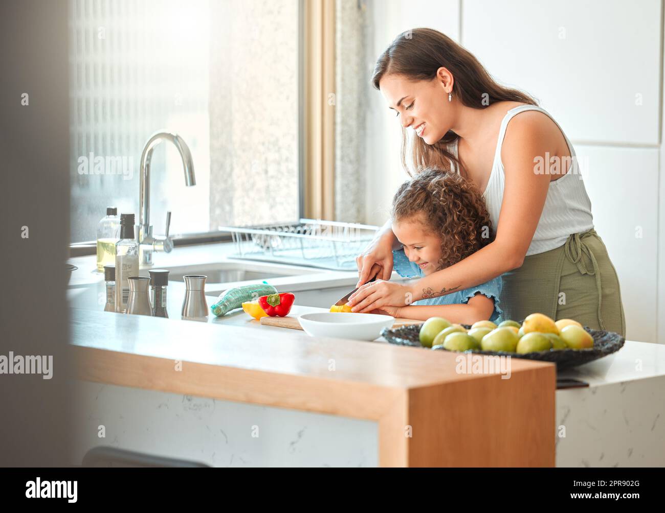 Madre cariñosa e hija pequeña que corta verduras y que prepara una ensalada en la cocina en casa. Vínculo de la niña con la madre mientras aprende a cocinar Foto de stock