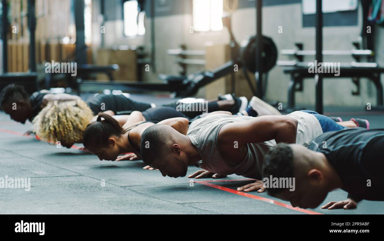 Un poco más de empuje cada vez. Un grupo de jóvenes deportistas haciendo pushups juntos en un gimnasio. Foto de stock