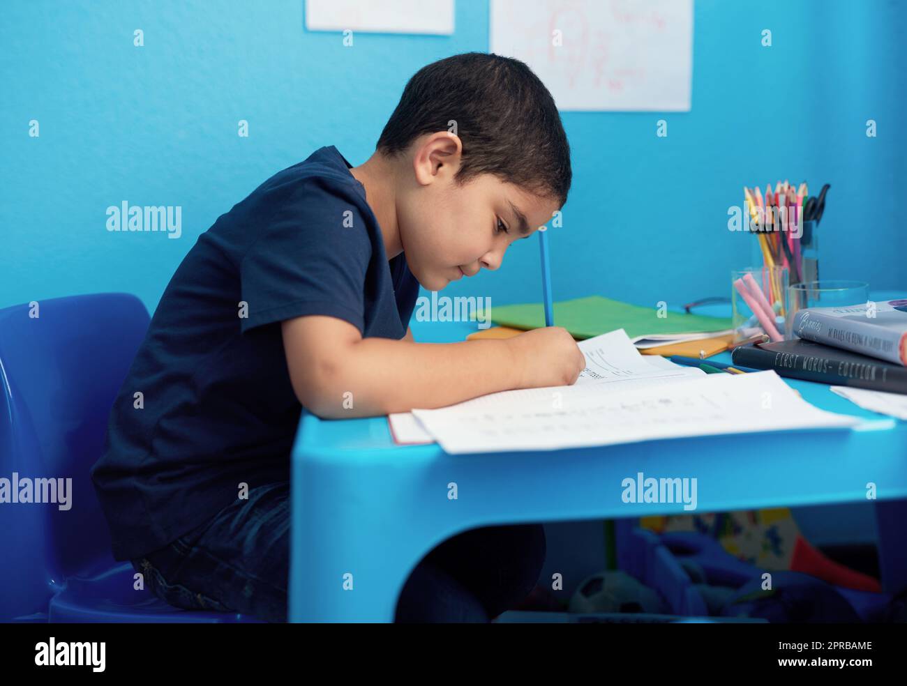 Estoy dibujando éste para mamá. Un adorable niño completando una asignación escolar en su escritorio. Foto de stock