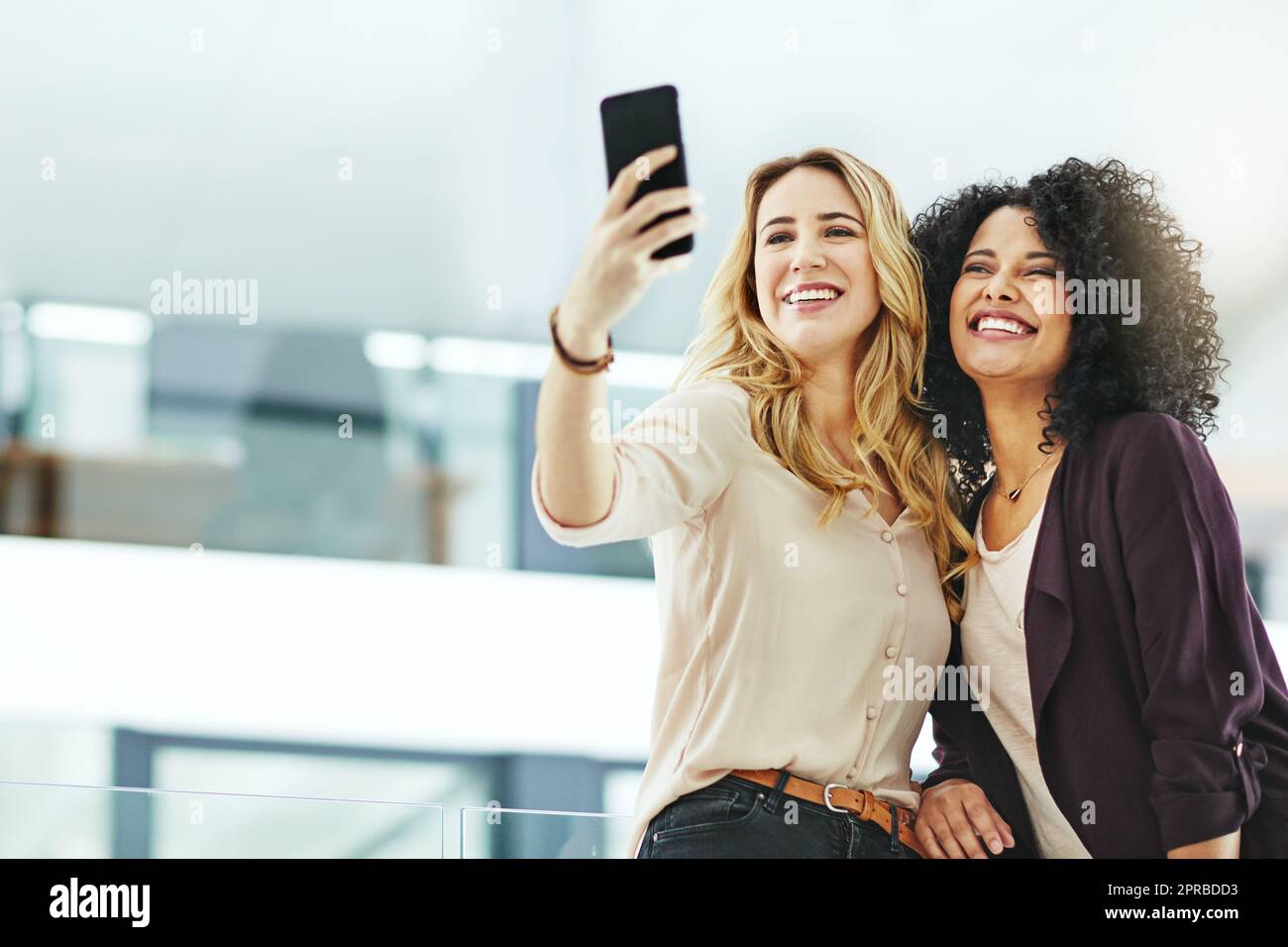 Mujeres felices, sonrientes y alegres tomando selfies con un teléfono mientras se unen, se divierten y se despreocupan en el trabajo. Colegas diversos, alegres y positivos que toman fotos para las redes sociales Foto de stock