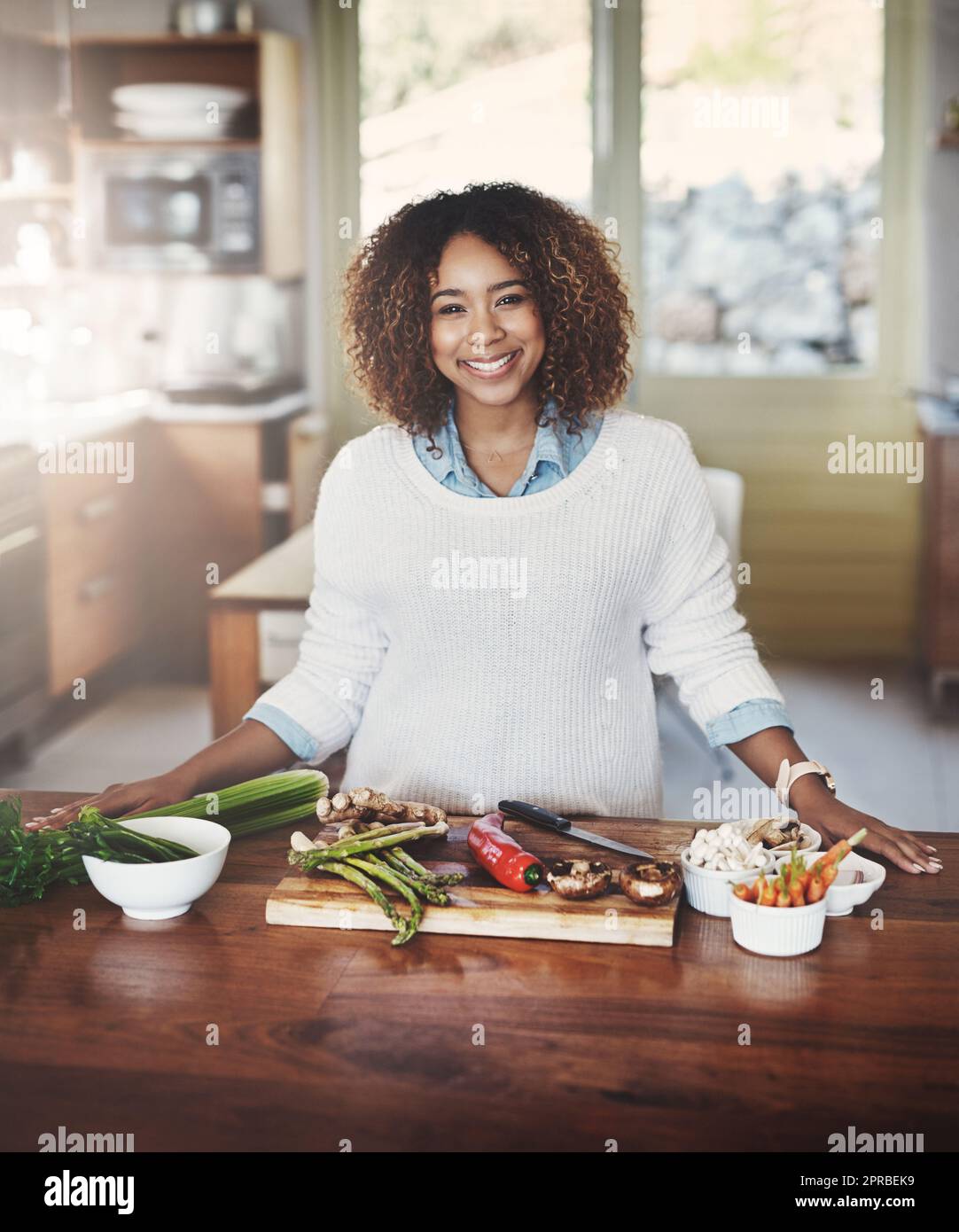 Retrato de mujer negra feliz que prepara la comida sana en una cocina en casa. Joven afroamericano que utiliza verduras frescas para hacer una deliciosa y equilibrada comida baja en carbohidratos. Señora en una dieta de limpieza y desintoxicación Foto de stock
