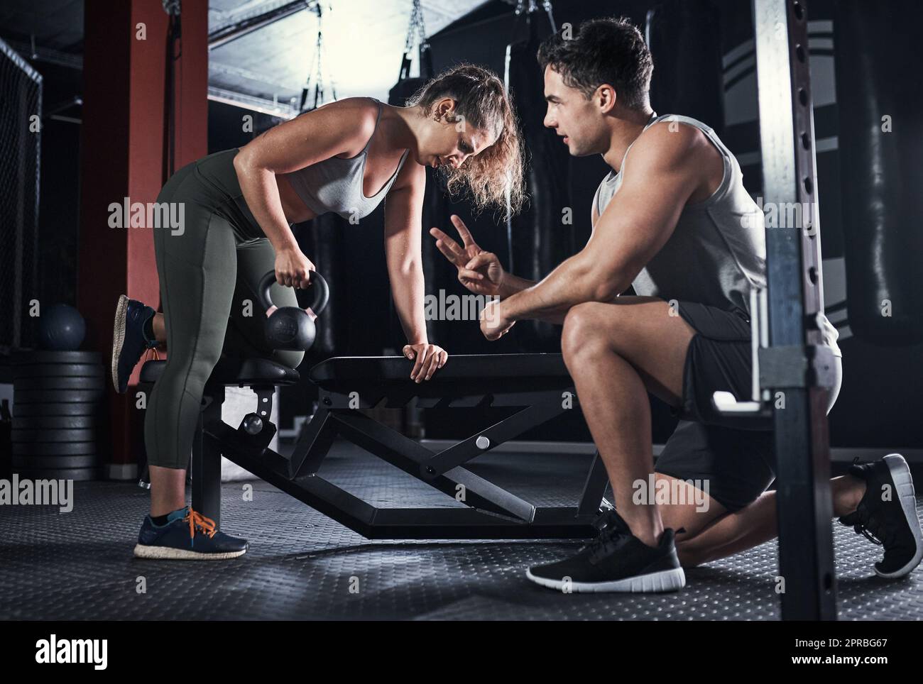 Sólo unos pocos más. Una mujer joven deportiva que hace ejercicio con un instructor de fitness en un gimnasio. Foto de stock