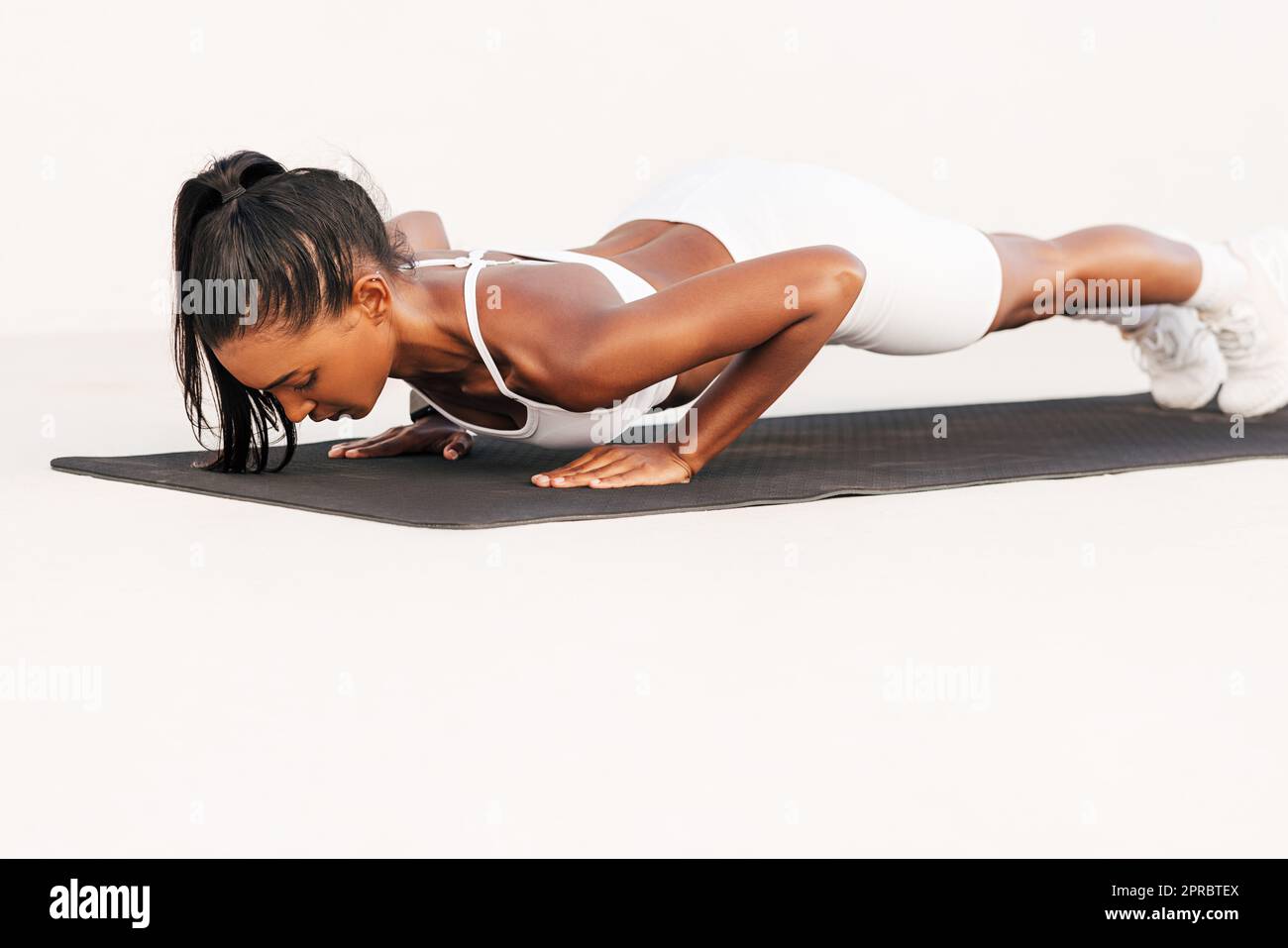 Mujer muscular delgada haciendo flexiones en una estera en el estudio blanco al aire libre. Atleta profesional que hace ejercicio en una esterilla haciendo un entrenamiento del core. Foto de stock