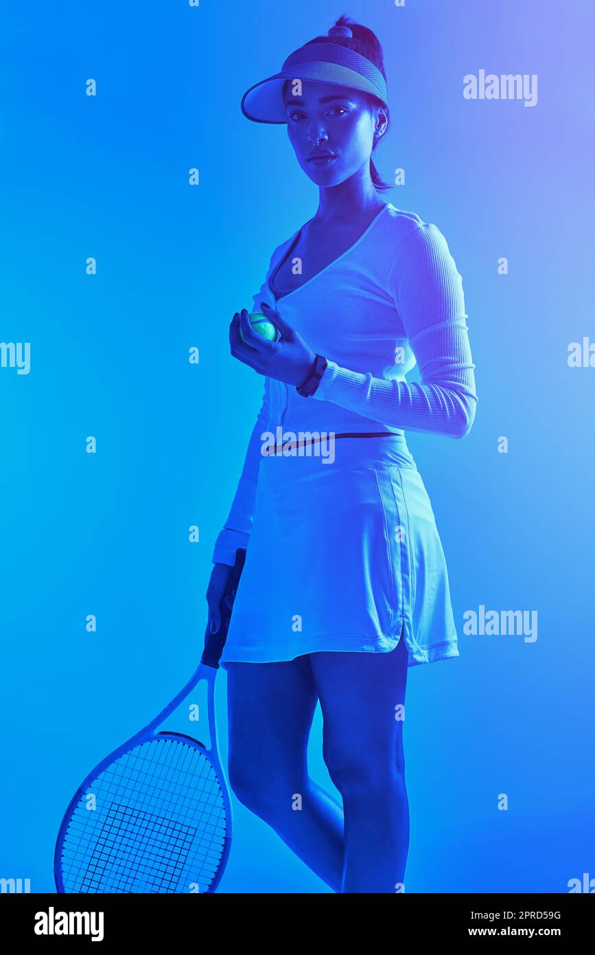 Trabajando en mi juego de tenis. Retrato recortado de una atractiva jugadora de tenis posando sobre un fondo azul. Foto de stock